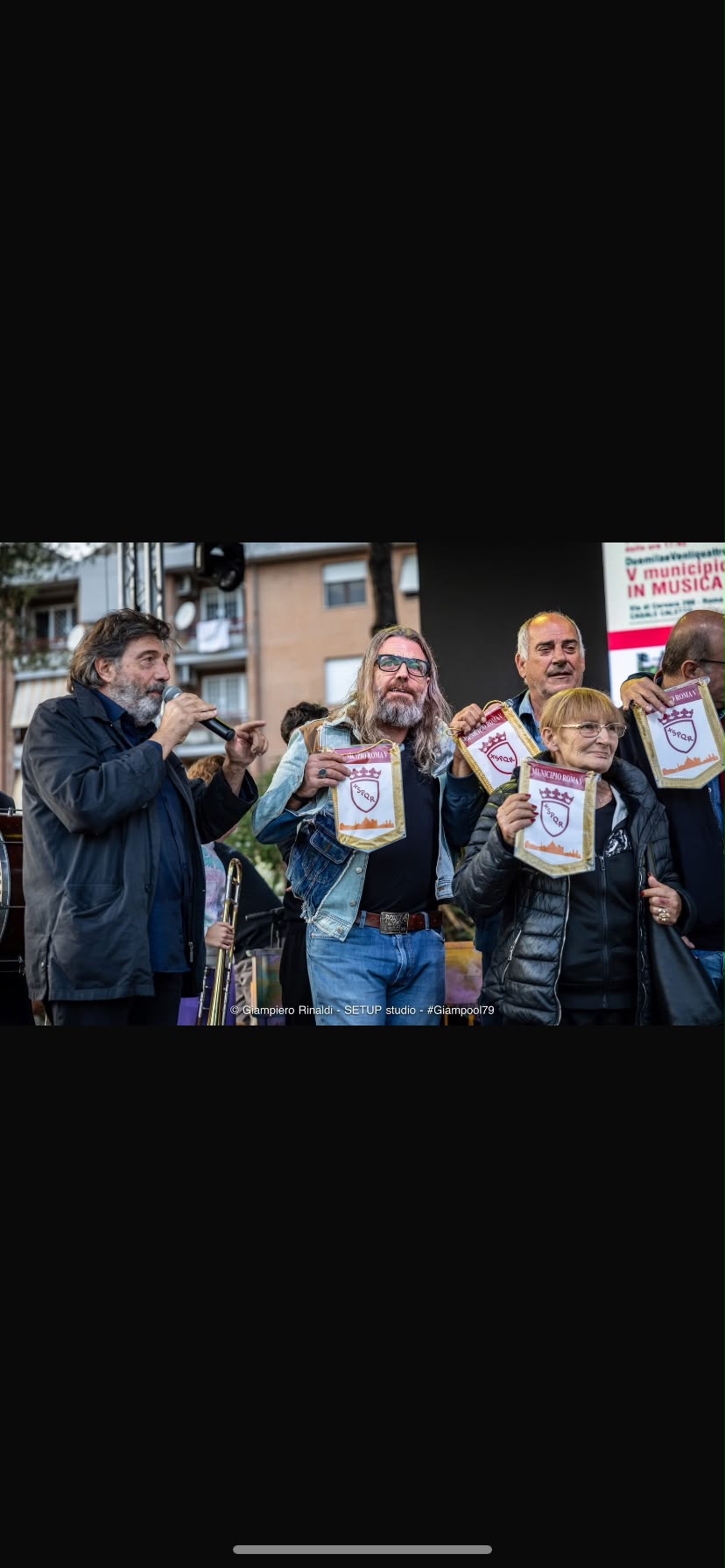 Mirko Frezza parla al microfono sul palco, accanto ad altre persone