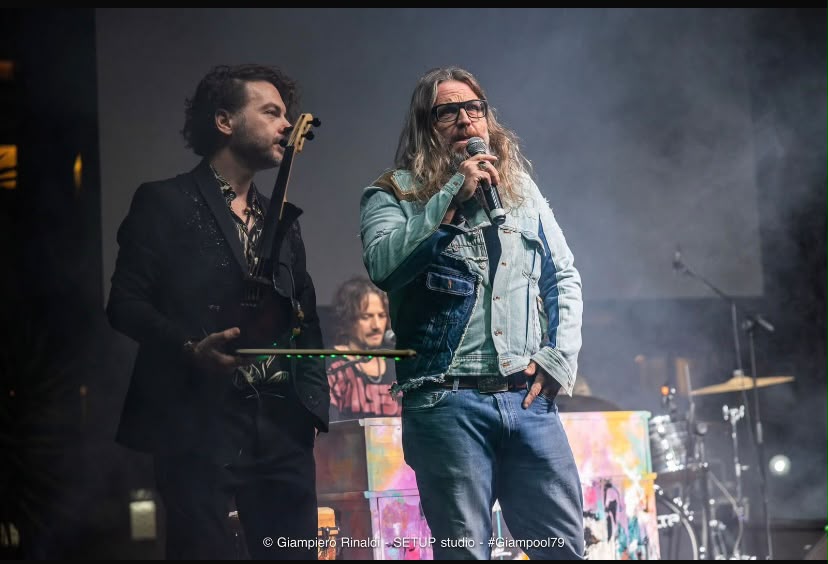 Un musicista e un ospite parlano sul palco, davanti a una batteria